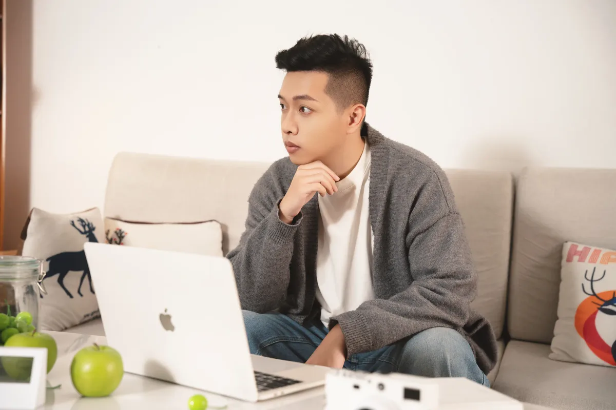 Jimmy 在自然光下坐在沙發前思考,桌上放著 MacBook;既有真實生活肖像