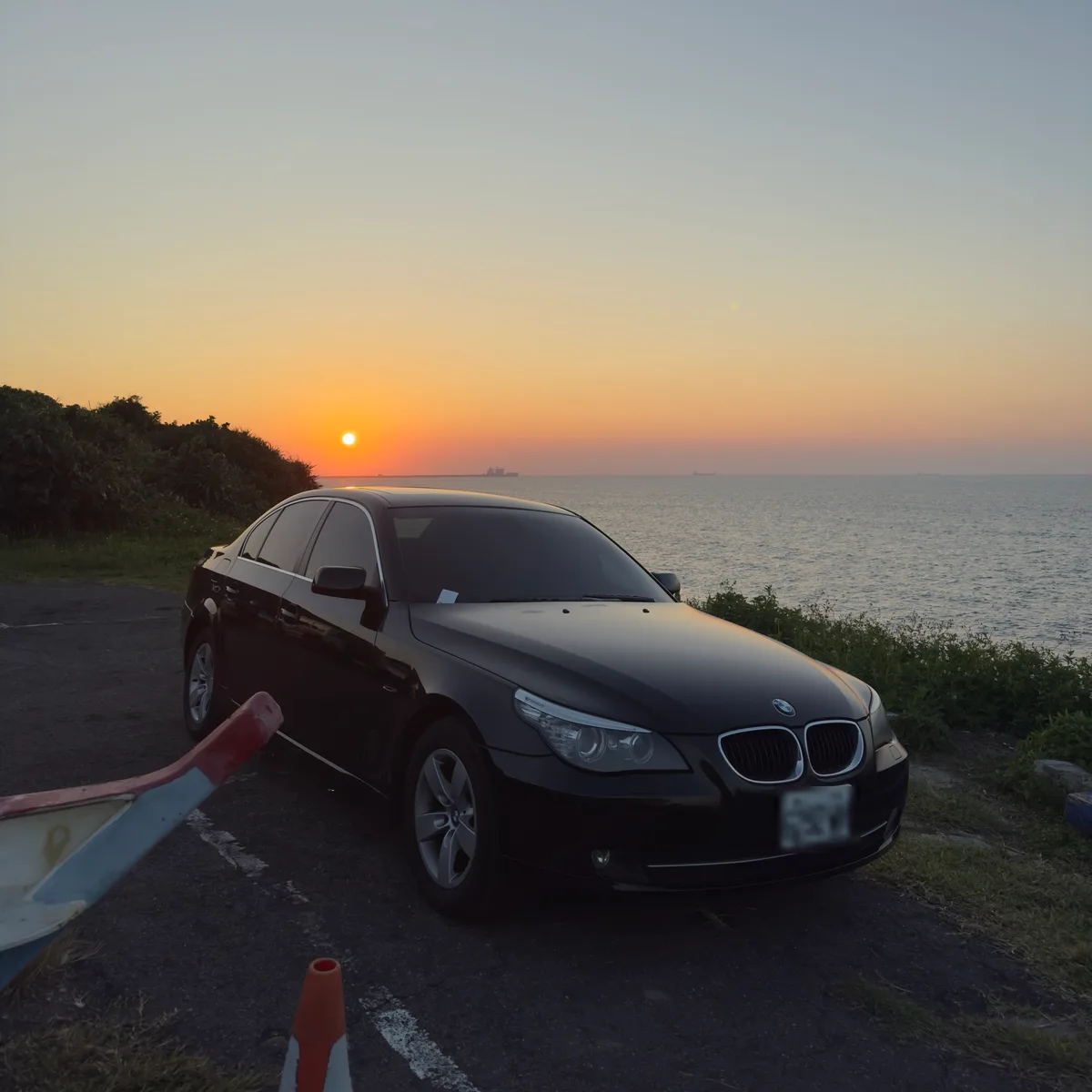 黑色 BMW E60 520d 停在海邊的觀景平台,前方是日落中的海平面
