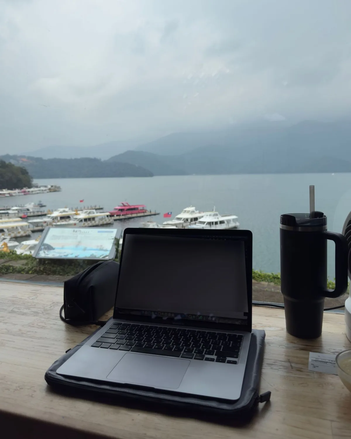 面湖吧台桌上的 MacBook,窗外是日月潭與碼頭遊艇