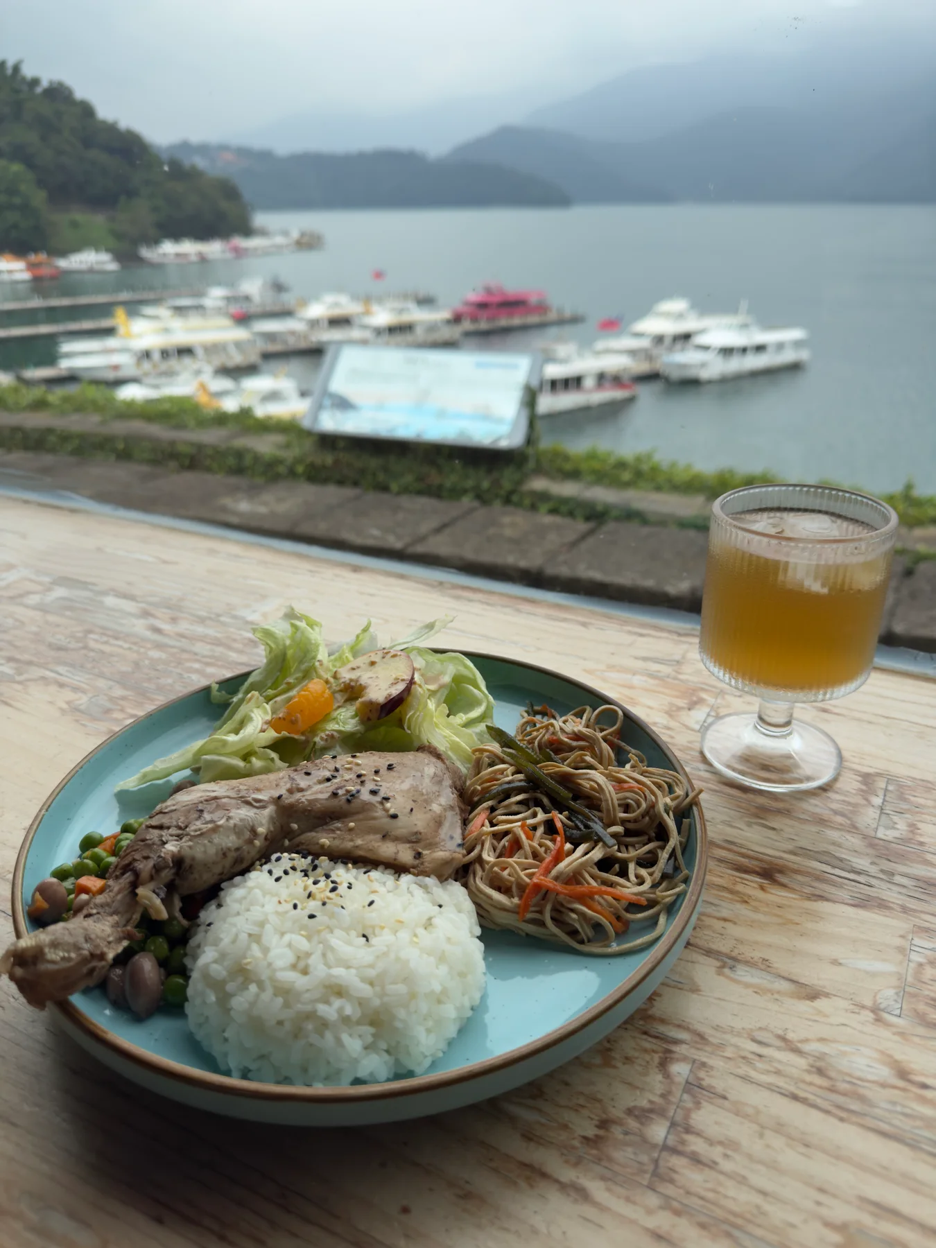 窗邊木桌上的雞腿飯與無糖麥茶,後方是日月潭碼頭