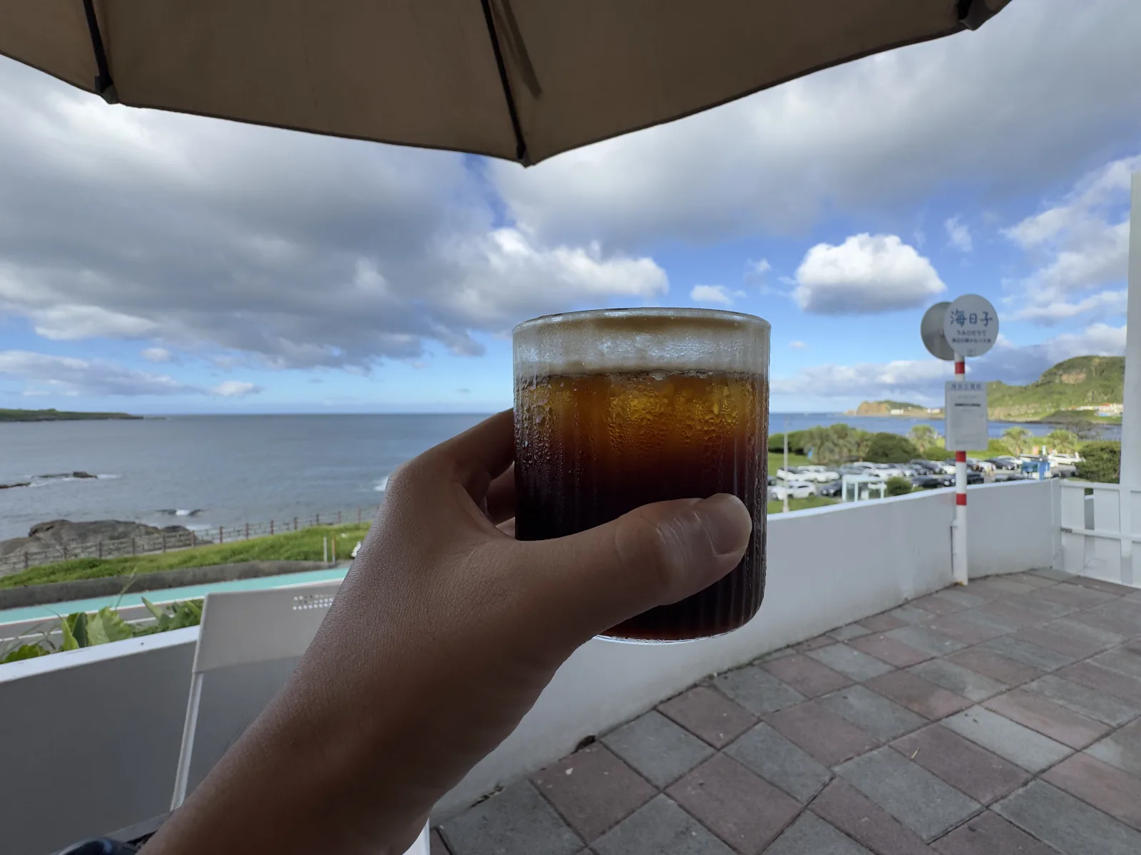 手舉著一杯冰咖啡,背景是北海岸的海與天空