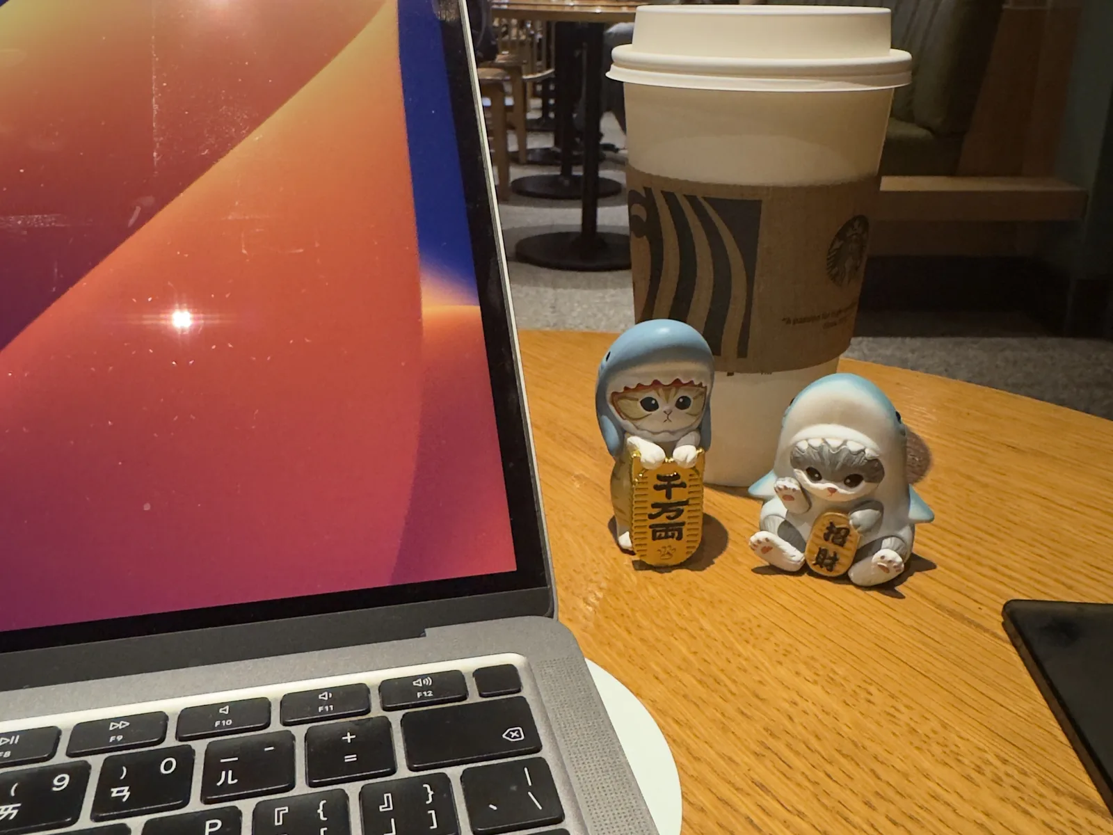 咖啡廳木桌上的 MacBook、咖啡杯與兩個小公仔