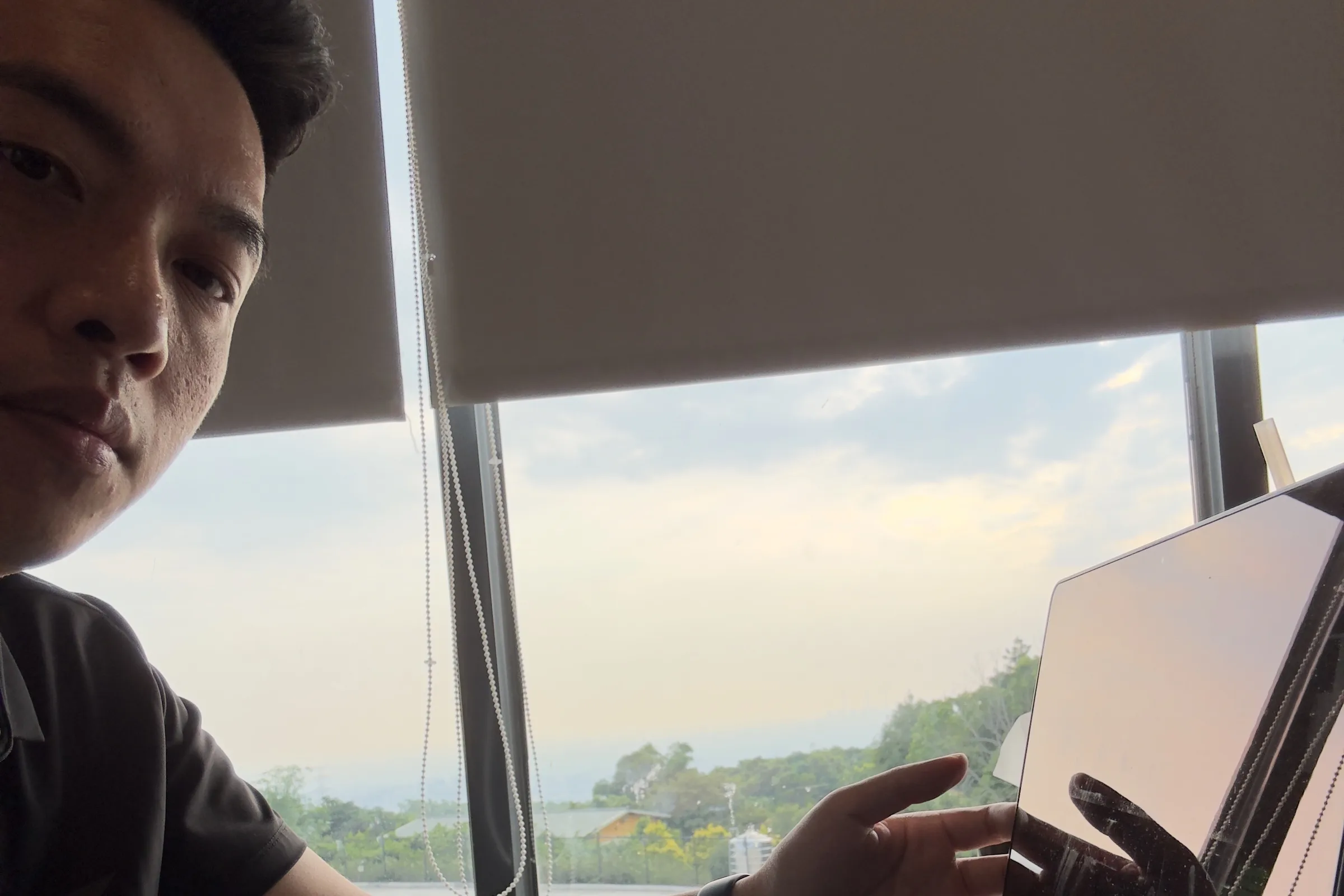 Jimmy 坐在咖啡廳窗邊,手放在 MacBook 上,窗外是樹林與天空