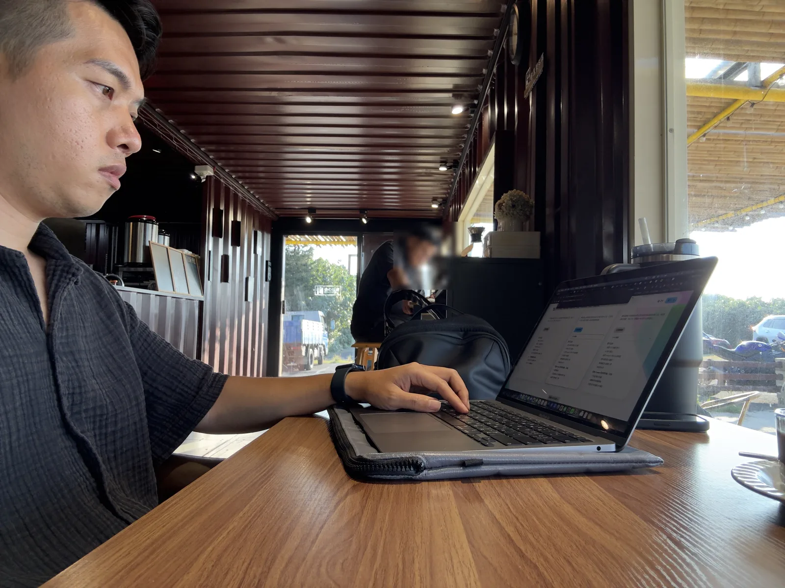 Jimmy 坐在貨櫃屋室內的長桌前使用 MacBook 工作,室內是深色貨櫃內裝