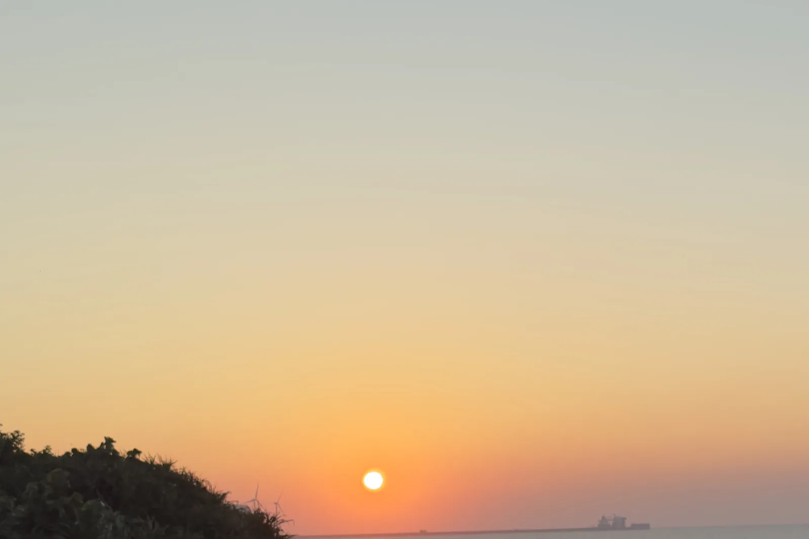 太陽正要沉入海平面,天空從橘色漸層到藍色,遠方有一艘貨輪